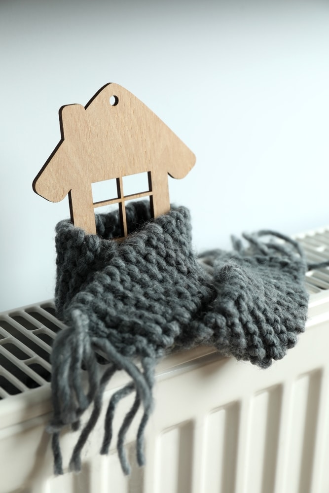 Chauffage et isolation : maison au chaud sur un radiateur Maison en bois avec écharpe grise sur un radiateur blanc, symbolisant le chauffage et l'isolation thermique.
