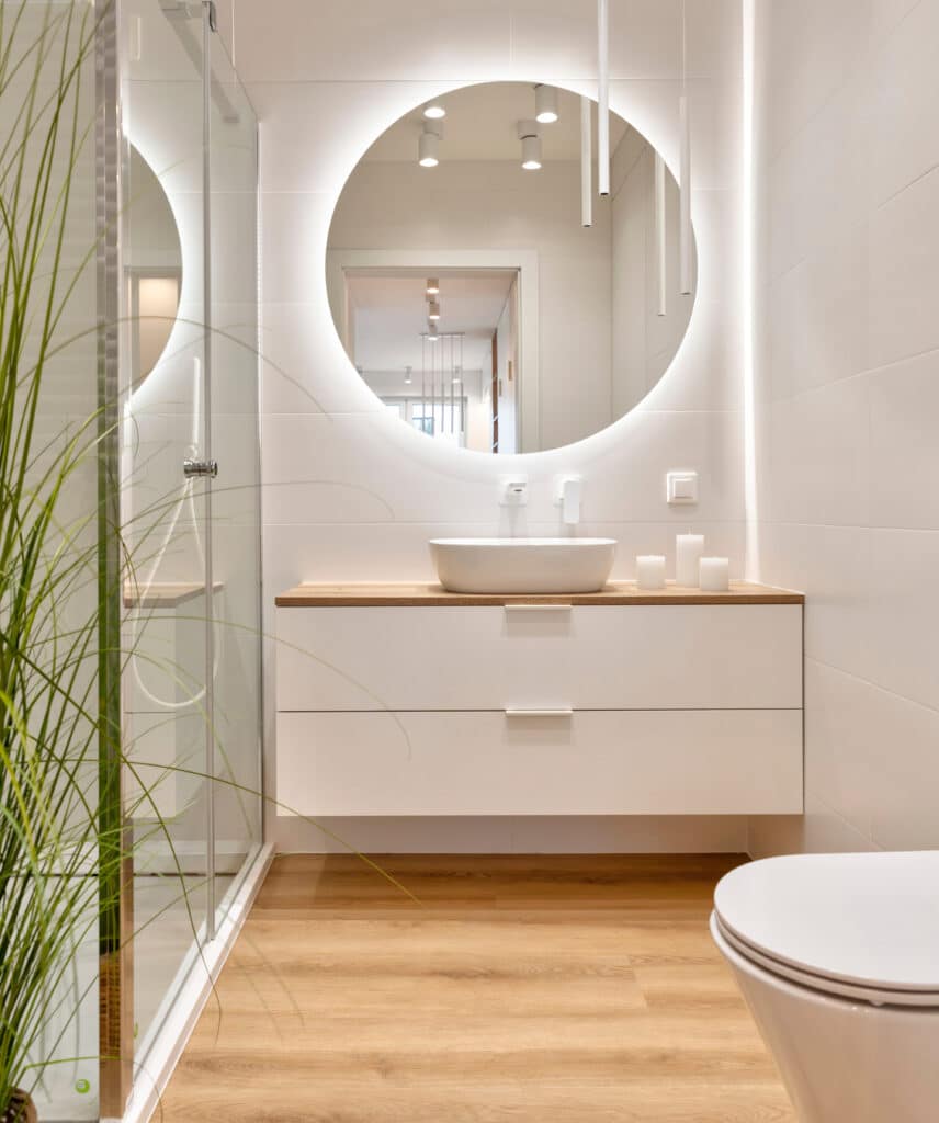 Aménagement Salle de Bain Moderne avec Miroir Lumineux Salle de bain moderne avec miroir rond rétroéclairé, vasque blanche sur meuble suspendu et sol en bois clair.